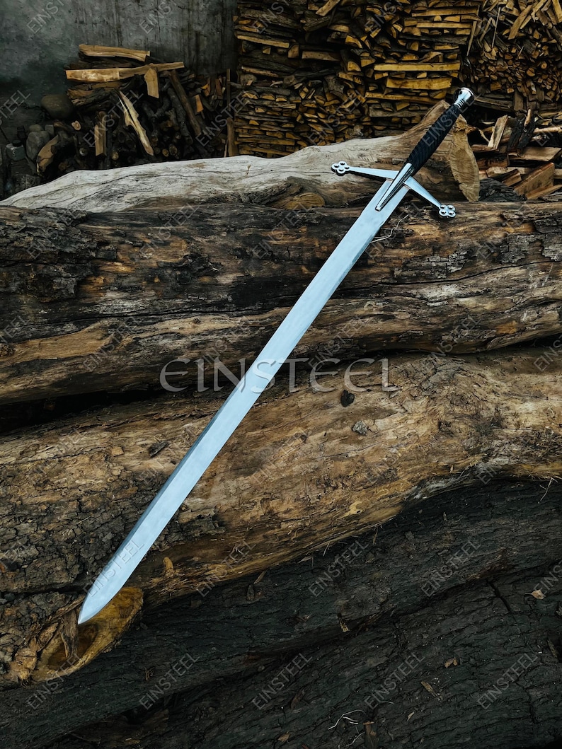 May include: A long, silver sword with a black handle and crossguard, resting on a weathered wooden log. The blade is sharp and reflective, with a pointed tip. The crossguard has a decorative design. The background features more wood.