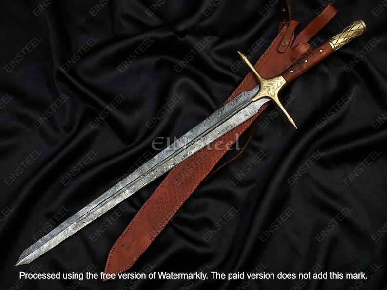 May include: A long, ornate sword with a patterned blade and gold-colored hilt, resting in a brown leather sheath. The sword features a crossguard and a wooden handle. The background is a dark, textured fabric.