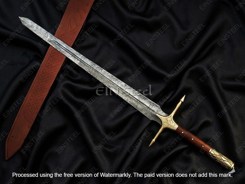 May include: A long, ornate sword with a patterned blade, gold crossguard, and a dark wooden handle. The sword rests on a black fabric with a brown leather strap. The blade has a length of approximately 30 inches.