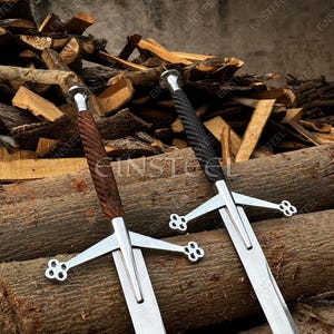 May include: Two medieval swords with silver blades and cross-shaped hilts. One sword has a brown, twisted handle, and the other has a black, twisted handle. The swords are displayed against a backdrop of stacked logs.
