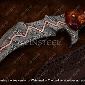 Pu&ograve; includere: Un coltello curvo con lama in acciaio damasco caratterizzato da un intarsio in rame a zigzag. Il manico &egrave; realizzato in resina lucida color bruno-rossastro con tre rivetti circolari in ottone. La lama presenta una punta affilata e un filo curvo.