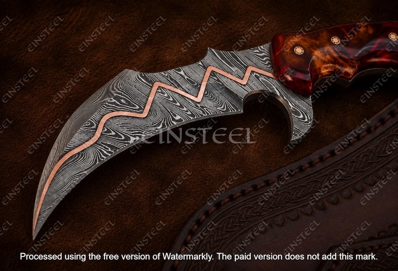 Pu&ograve; includere: Un coltello curvo con lama in acciaio damasco caratterizzato da un intarsio in rame a zigzag. Il manico &egrave; realizzato in resina lucida color bruno-rossastro con tre rivetti circolari in ottone. La lama presenta una punta affilata e un filo curvo.