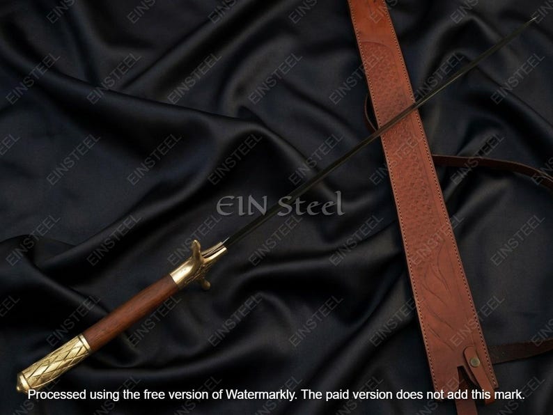 May include: A sword with a dark blade, wooden handle, and gold-colored accents. The sword rests on a black fabric surface, accompanied by a brown leather sheath. The text "EIN Steel" is visible.