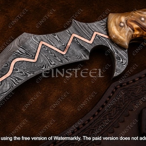 Pu&ograve; includere: Un coltello curvo con lama in acciaio damasco a motivi, caratterizzato da un intarsio in rame a zig-zag. Il manico &egrave; realizzato in materiale lucidato e marmorizzato nei toni del marrone e crema, fissato con due perni metallici.