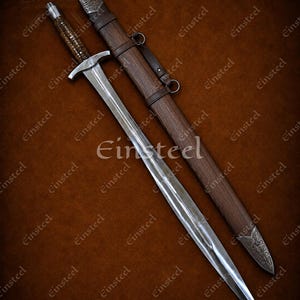May include: A steel sword with a textured brown grip and a silver crossguard, accompanied by a matching brown wooden scabbard featuring dark leather straps and an ornate silver metal tip with intricate engraved detailing on the surface.
