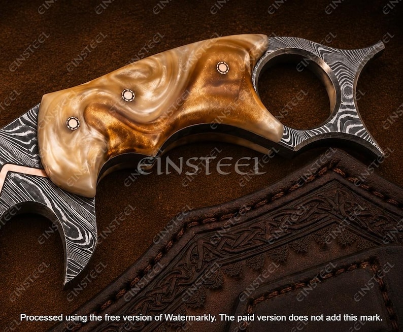 Pu&ograve; includere: Un coltello karambit con una lama in acciaio Damasco a motivi e un manico in resina lucida con vortici color marrone chiaro e crema. Il manico &egrave; fissato con tre rivetti metallici circolari e include un grande anello per il dito.