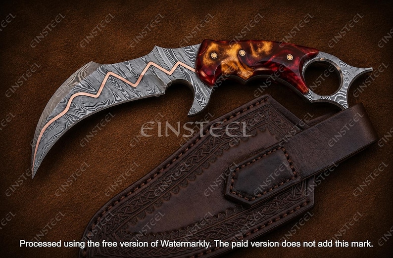 Pu&ograve; includere: Un coltello karambit curvo con lama in acciaio damasco caratterizzata da una linea a zigzag in rame intarsiato. L'impugnatura &egrave; in resina marmorizzata rossa e ambra con tre perni in ottone e un anello per il dito sul pomolo. Fodero incluso.