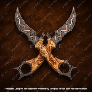 Op de afbeelding: Twee gekruiste karambit-messen met damaststalen bladen met een centrale koperen zigzag-inleg. De handgrepen zijn gemaakt van gepolijst lichtbruin wortelhout, elk vastgezet met drie metalen klinknagels, en zijn voorzien van een vingerring.