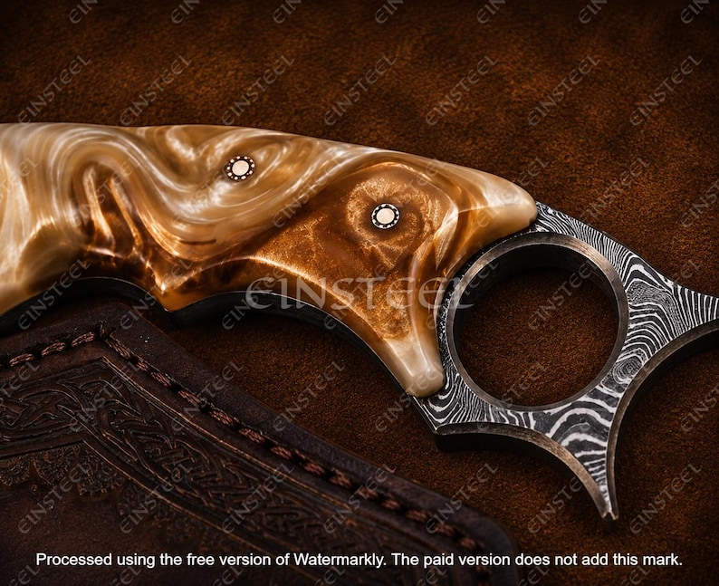 Pu&ograve; includere: Un coltello karambit con un manico dal motivo marmorizzato marrone e crema, fissato da due rivetti metallici circolari. La lama presenta un distinto motivo in acciaio damasco e include un prominente anello per le dita alla base.
