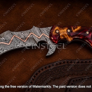 Pu&ograve; includere: Un coltello karambit curvo con lama in acciaio Damasco e un intarsio in rame a zigzag. Il manico &egrave; realizzato in resina lucida rossa e ambra con tre rivetti metallici. Un anello per il dito &egrave; integrato nell'estremit&agrave; del pomolo.