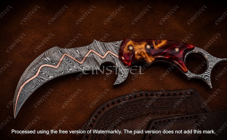 Pu&ograve; includere: Un coltello karambit curvo con lama in acciaio Damasco e un intarsio in rame a zigzag. Il manico &egrave; realizzato in resina lucida rossa e ambra con tre rivetti metallici. Un anello per il dito &egrave; integrato nell'estremit&agrave; del pomolo.
