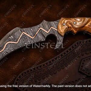 Pu&ograve; includere: Un coltello karambit curvo con lama in acciaio Damasco caratterizzata da un inserto in rame a zigzag, manico in resina marrone marmorizzata con tre rivetti argentati e anello per il dito sul pomolo, accompagnato da un fodero in pelle scura.