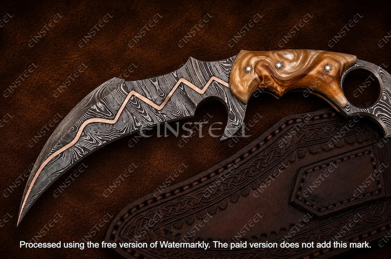 Pu&ograve; includere: Un coltello karambit curvo con lama in acciaio Damasco caratterizzata da un inserto in rame a zigzag, manico in resina marrone marmorizzata con tre rivetti argentati e anello per il dito sul pomolo, accompagnato da un fodero in pelle scura.