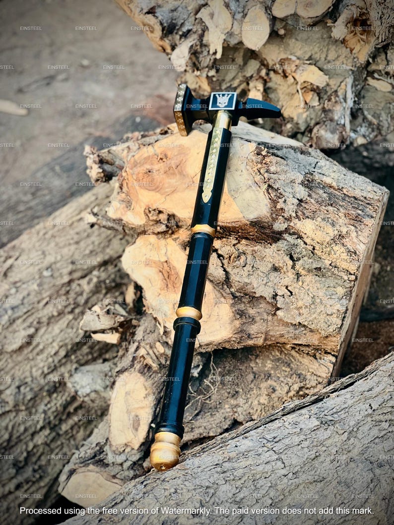 May include: A black and gold hammer with a decorative handle. The hammerhead is square with a symbol in the center. The handle is black with gold accents and a gold base. The hammer is resting on a piece of wood.