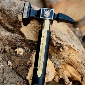 May include: A black and gold hammer with a skull and crown design on the head. The hammer has a wooden handle with brass accents. The image is set against a wood background. The text "EINSTEEL" is repeated throughout the image.
