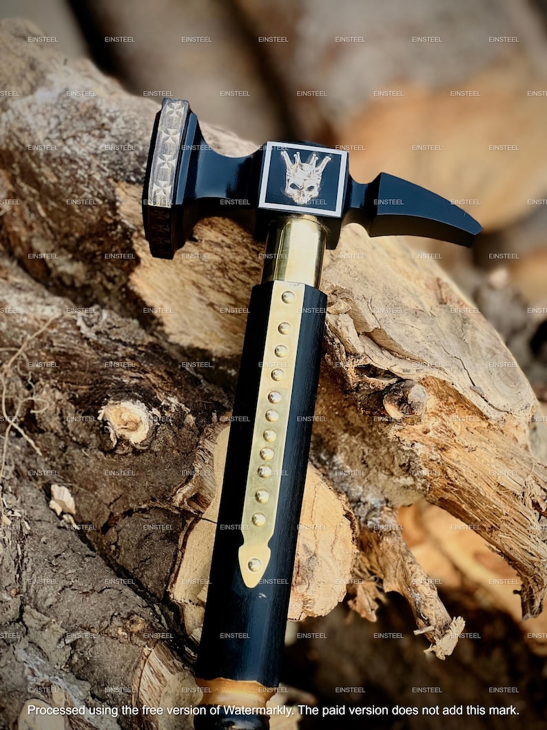 May include: A black and gold hammer with a skull and crown design on the head. The hammer has a wooden handle with brass accents. The image is set against a wood background. The text "EINSTEEL" is repeated throughout the image.