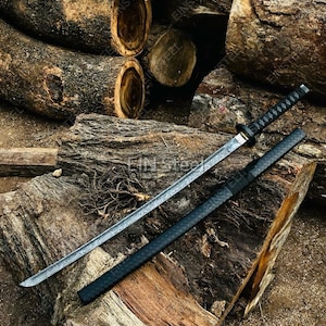 May include: A katana sword with a patterned steel blade and a black wrapped handle, accompanied by a matching black textured scabbard. The blade features a visible wavy temper line, and the hilt includes a circular guard, resting on wood.