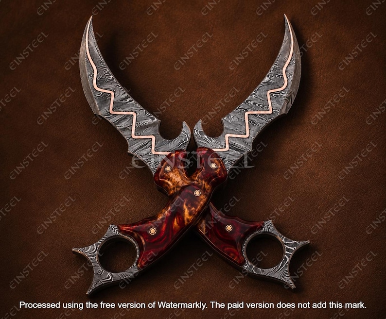 Pu&ograve; includere: Due coltelli karambit incrociati con lame in acciaio Damasco e intarsio in rame ondulato. I manici sono realizzati in legno radica bruno-rossastro lucidato con perni in ottone e anelli per le dita integrati alla base di ogni manico.