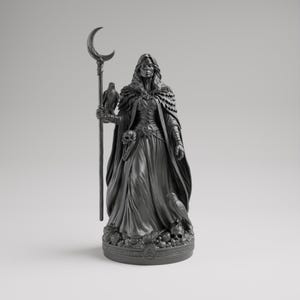 Op de afbeelding: Een donkergrijze beeld van een geklede figuur die een staf vasthoudt met een halve maan aan de bovenkant. Een vogel zit op de staf en een andere aan de basis. De figuur draagt een mantel en heeft een schedel op de riem.