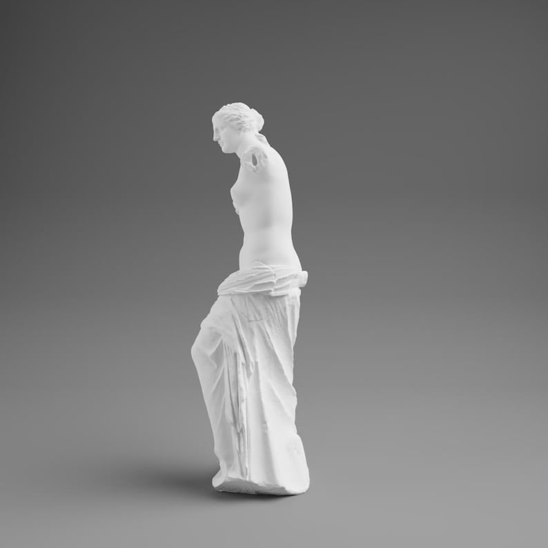 May include: A white plaster statue of Venus de Milo, a classical sculpture. The statue is missing both arms and stands draped in fabric. The figure is set against a gray background, showcasing the details of the sculpture.