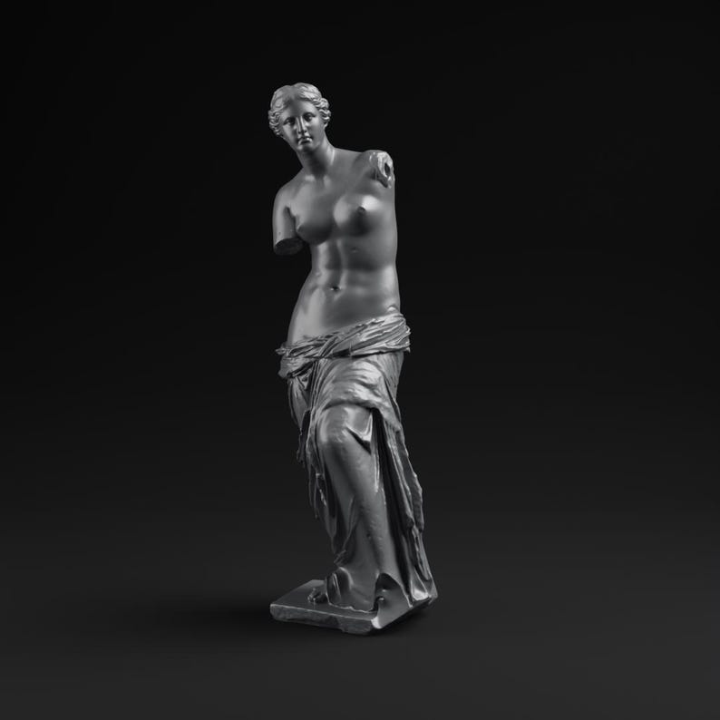 May include: A gray sculpture of a classical female figure, missing both arms. The statue is draped in fabric around the lower body and stands on a rectangular base. The background is black.
