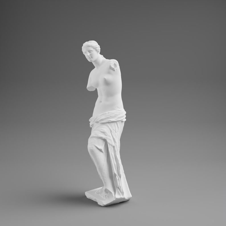 May include: A white plaster statue of Venus de Milo, a classical sculpture. The statue is missing both arms and stands draped in fabric. The sculpture is set against a gray background.