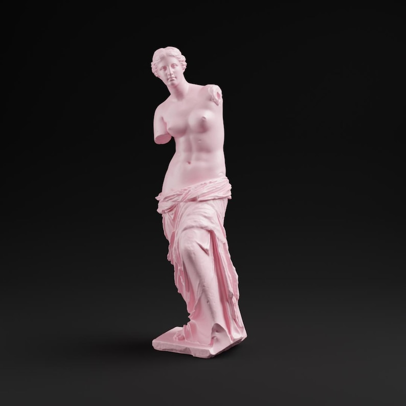 May include: A pink statue of Venus de Milo, a classical sculpture, stands against a black background. The statue is missing both arms and is draped in fabric around the lower body. The sculpture is a solid pink color.