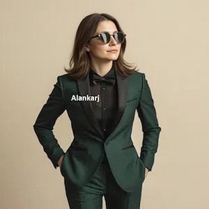 May include: A dark green blazer with black lapels, a black button-down shirt, and a black bowtie. The word Alankarj is printed on the left side of the blazer. The outfit is paired with dark sunglasses featuring round frames and dark lenses.