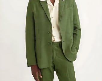 May include: A green suit, comprising a blazer and trousers, worn with a cream-coloured button-down shirt. The blazer features a two-button fastening and a notched lapel. The outfit is a solid colour, with a tailored fit.