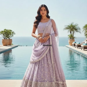 May include: A lilac formal gown with detailed embroidery and a matching sheer scarf. The outfit features a crop top and a full skirt. The image is set against a backdrop of a pool and ocean, with the text "Alankari" visible.