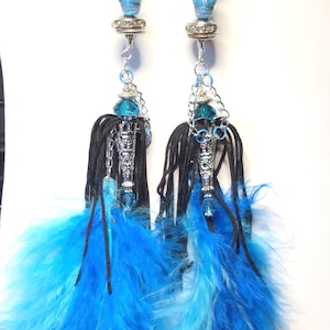 May include: A pair of long, blue feather earrings with a silver skull charm and blue crystal beads. The earrings are hanging from a silver hook.