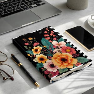 Floral pattern notebook with pen, glasses, phone, and laptop.