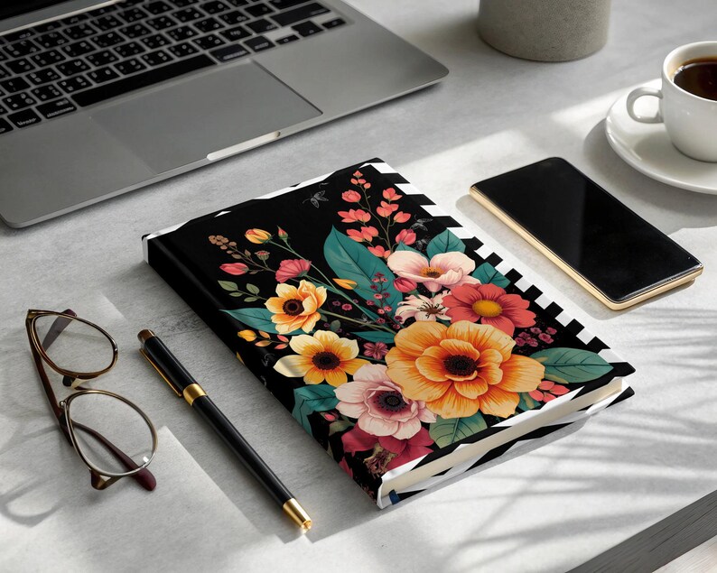 Floral pattern notebook with pen, glasses, phone, and laptop.