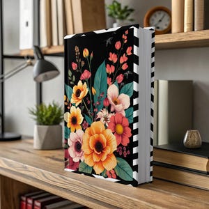 Black book with vibrant floral cover illustration, displayed on a wooden shelf.