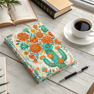 May include: A floral journal with a cactus design, featuring orange, teal, and yellow flowers on a white background. The journal is open on a wooden table, with a cup of coffee, a pen, and books.
