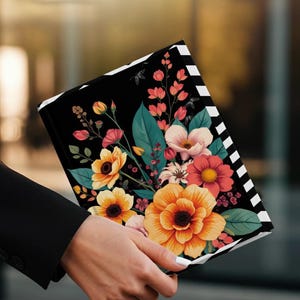 Black notebook with colorful floral design held by a person in a black jacket.