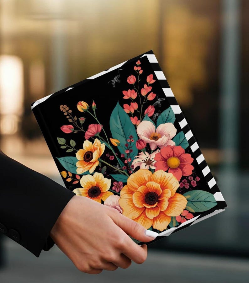 Black notebook with colorful floral design held by a person in a black jacket.