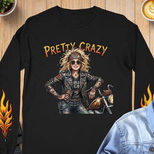 May include: Black long-sleeve shirt with a graphic of a woman in a leather jacket, sunglasses, and a motorcycle. The text "PRETTY CRAZY" is above the graphic. Flames are on the sleeves.