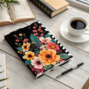 Black notebook with colorful floral design and striped border, next to coffee.
