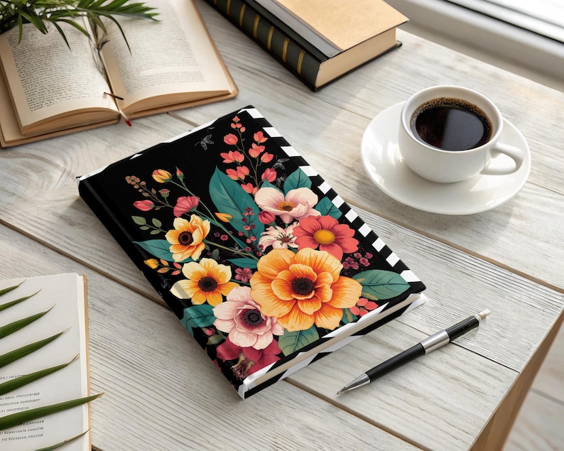 Black notebook with colorful floral design and striped border, next to coffee.