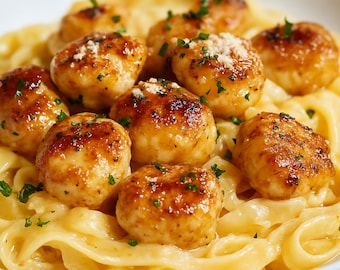 May include: A close-up shot of a plate of pasta with meatballs. The meatballs are golden brown and topped with a sprinkle of cheese and herbs. The pasta is coated in a creamy sauce.