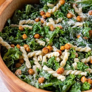 Puede incluir: Un bol de madera lleno de una ensalada de col rizada, pasta, garbanzos y un aderezo cremoso blanco.