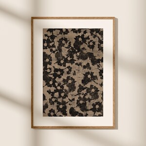 以下が含まれることがあります： ベージュの背景に黒と白の花柄がプリントされた額装されたプリント。プリントはシンプルな木製フレームに入っています。