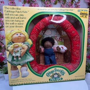Può includere: Set di bambole Cabbage Patch Kids da collezione nella confezione originale. La scatola presenta una bambola bionda che tiene in mano una bambola più piccola e una bambola nera all'interno di una cornice a forma di cuore rosso. La scatola riporta la scritta "Cabbage Patch Kids PIN-UPS".