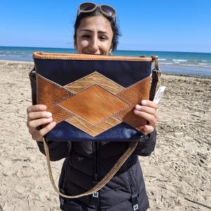 Puede incluir: Bolso rectangular con diseño geométrico. El bolso presenta una parte superior e inferior azul marino, con una sección central de cuero marrón y beige en un patrón de diamantes. Se adjunta una correa dorada.