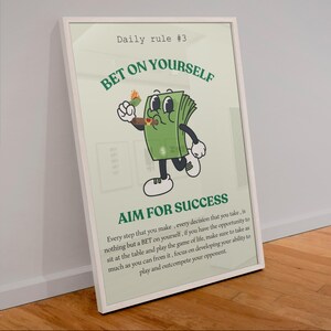 Può includere: Un poster incorniciato con il testo "Daily rule #3 BET ON YOURSELF AIM FOR SUCCESS". Il poster presenta un personaggio di banconota dei cartoni animati che tiene in mano un sigaro acceso. Lo sfondo è verde chiaro.