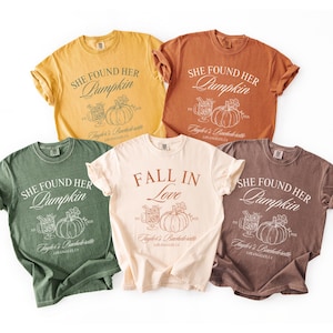 May include: Five short-sleeve crew neck t-shirts in yellow, orange, green, cream, and brown. Each shirt features a graphic print with the text "SHE FOUND HER PUMPKIN" or "FALL IN LOVE," along with illustrations of a pumpkin and a drink.
