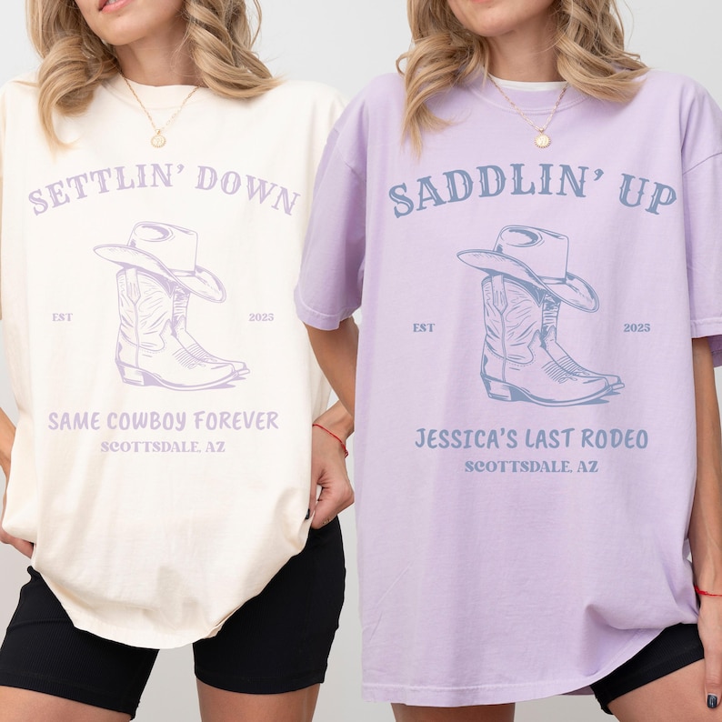 May include: Two short-sleeved t-shirts, one cream and one light purple, each featuring a graphic of a cowboy hat and boots. The cream shirt reads SETTLIN' DOWN, SAME COWBOY FOREVER, SCOTTSDALE, AZ. The purple shirt reads SADDLIN' UP, JESSICA'S LAST RODEO, SCOTTSDALE, AZ.