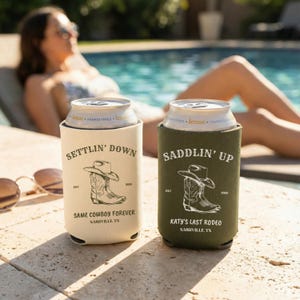May include: Two beverage insulators with cowboy-themed designs. One is beige with the text "Settlin' Down" and "Same Cowboy Forever, Nashville, TN." The other is olive green with "Saddlin' Up" and "Katy's Last Rodeo, Nashville, TN."