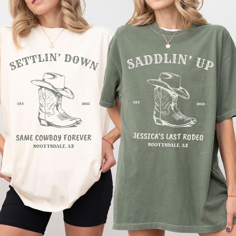May include: Two short-sleeve crew neck t-shirts, one cream and one sage green, each featuring a dark graphic of a cowboy boot and hat. The cream shirt reads SETTLIN' DOWN, SAME COWBOY FOREVER, SCOTTSDALE, AZ. The green shirt reads SADDLIN' UP, JESSICA'S LAST RODEO, SCOTTSDALE, AZ.